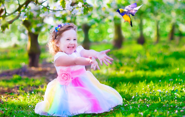 Смеющаяся маленькая девочка в красивом платье на зеленой траве