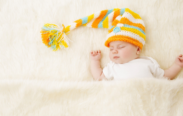 Маленький спящий под меховым покрывалом малыш в вязаной шапке