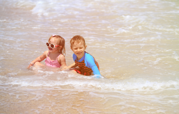 Маленькие мальчик и девочка купаются в море 