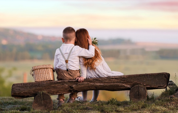 Маленькие мальчик и девочка обнимают друг друга на лавке