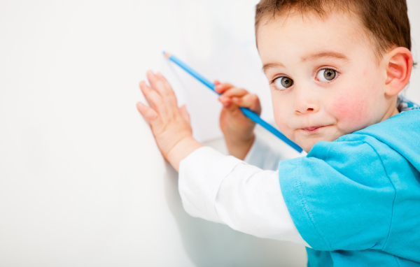 Маленький мальчик рисует карандашом на стене