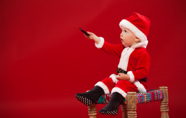 Маленький мальчик в костюме Санта Клауса сидит на стуле на красном фоне