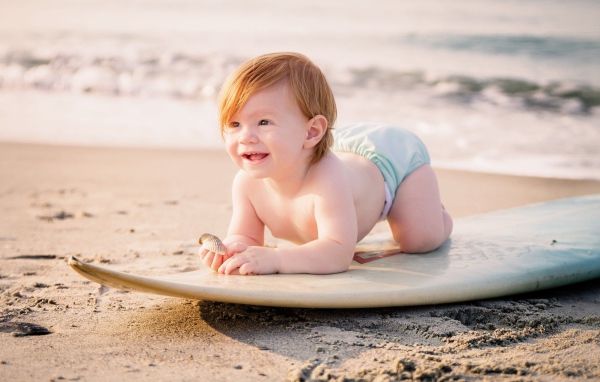 Маленький мальчик на доске для серфинга на пляже