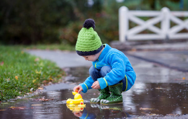 Маленький мальчик с резиновыми уточками в луже осенью