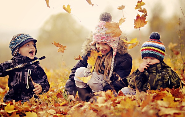 Маленькие дети играют на опавшей желтой листве осенью