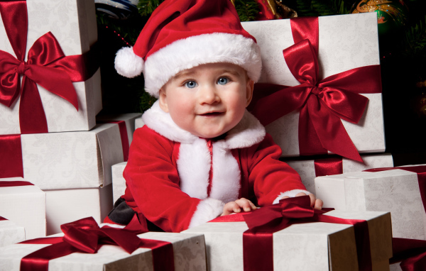 Маленький забавный голубоглазый ребенок в костюме Санты сидит на подарках