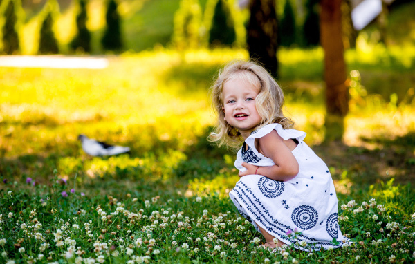 Маленькая девочка в красивом платье сидит на зеленой траве