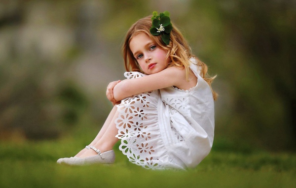 Маленькая девочка в белом платье сидит на зеленой траве