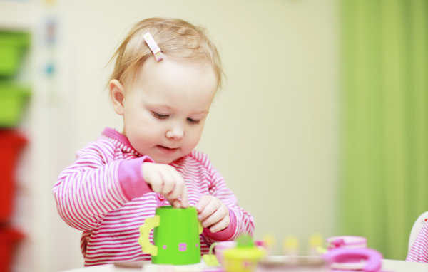 Маленькая девочка играет с посудой 