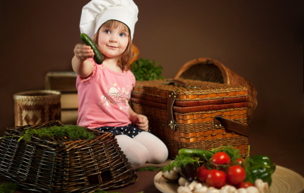 Маленькая девочка сидит на столе с корзинами и овощами