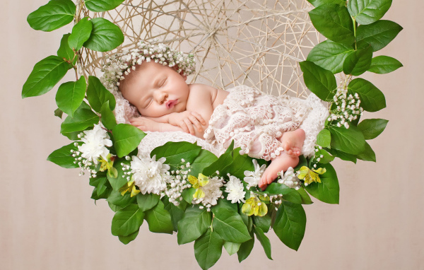 Маленькая девочка спит в колыбеле украшенной зелеными листьями