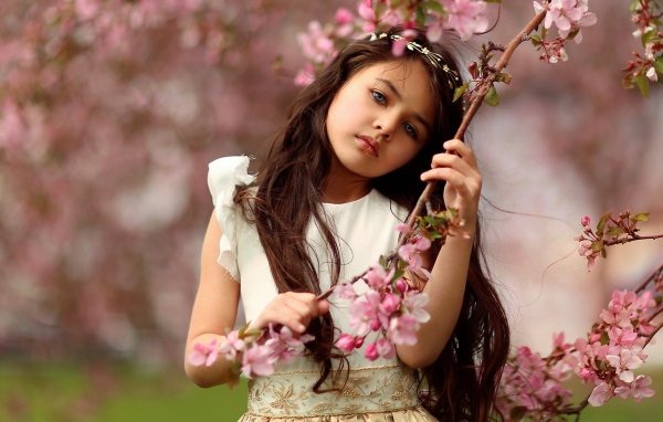 Маленькая девочка у цветущей розовыми цветами ветки