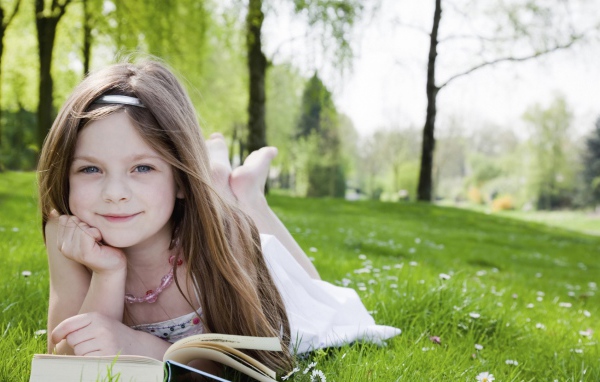 Маленькая девочка с книгой лежит на зеленой траве