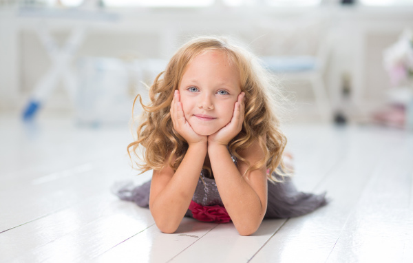 Маленькая длинноволосая голубоглазая девочка лежит на полу