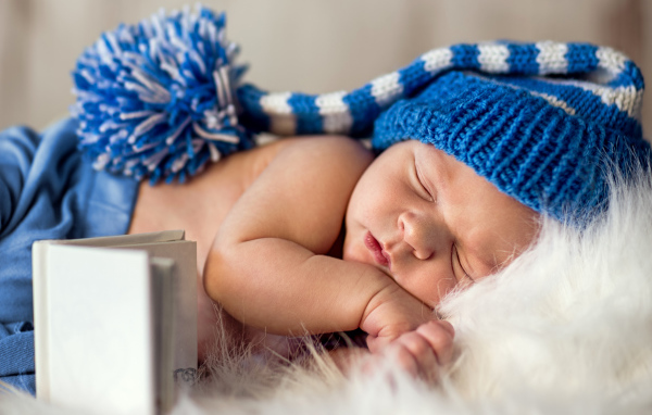 Маленький спящий грудной ребенок в синей вязанной шапке 