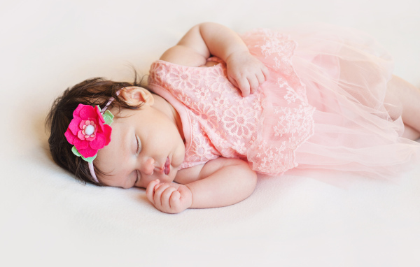 Маленькая спящая девочка в розовом платье с цветком в волосах 