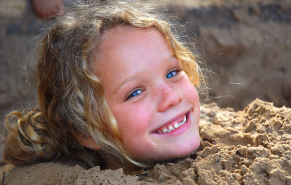 Маленькая улыбающаяся девочка играет в песке