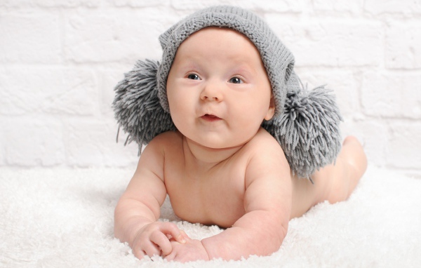 Улыбающийся грудной ребенок в серой шапке с бубонами