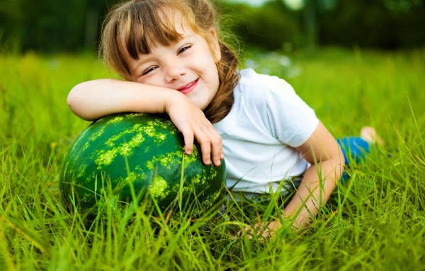 Улыбающаяся девочка с зеленым арбузом на траве