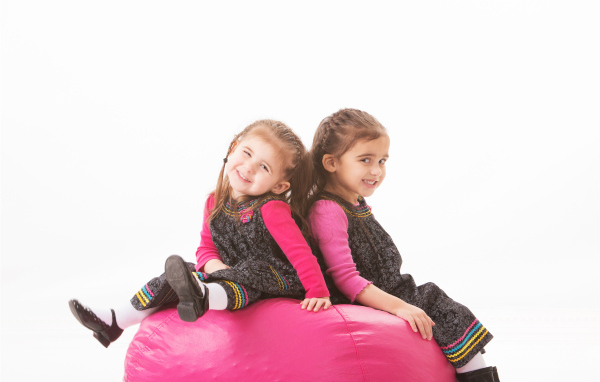 Две маленькие девочки сидят на красном мягком шаре 