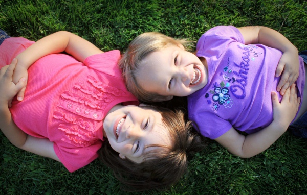 Две маленьких улыбающихся девочки лежат на зеленой траве