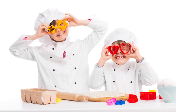 Два маленьких ребенка в костюмах повара готовят на кухне печенье
