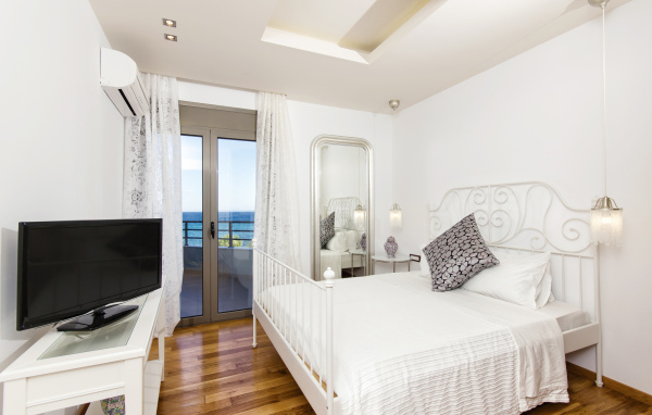 Светлая спальня с большой белой кроватью и телевизором 