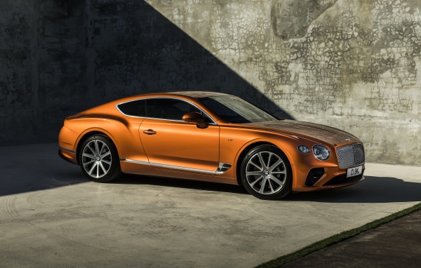 Оранжевый автомобиль Bentley Continental GT V8, 2019 года на фоне стены