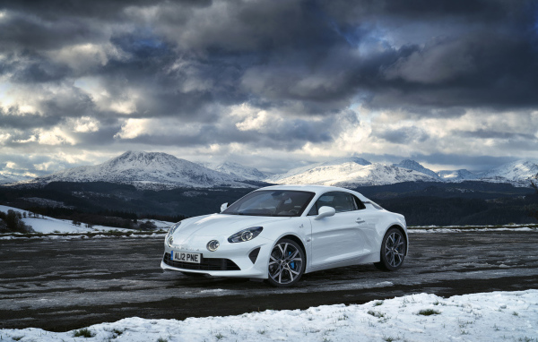 Белый автомобиль Alpine A110 на фоне гор под грозовым небом  