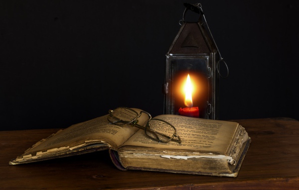Старая книга с очками на столе со свечой 
