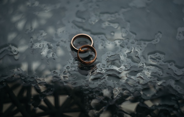 Два обручальных кольца лежат на мокрой черной поверхности 