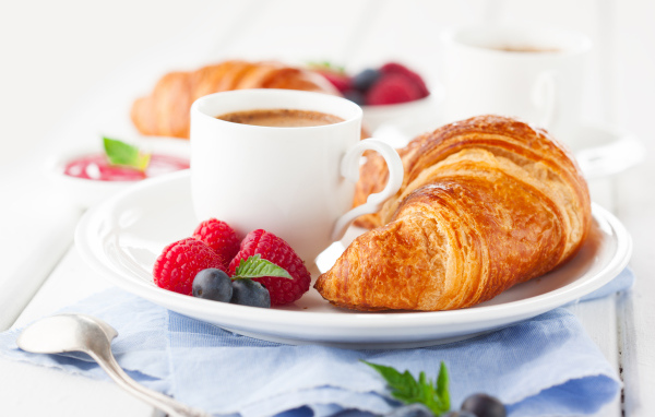 Чашка кофе на тарелке с круассаном и ягодами