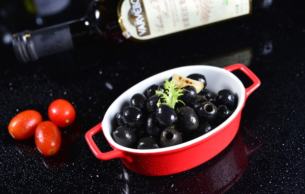 Черные оливки на столе с бутылкой и помидорами