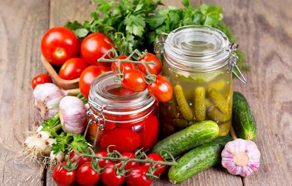 Консервированные помидоры и огурцы на столе со свежими овощами и зеленью 