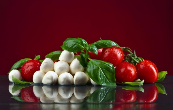 Сыр на столе с зеленью базилика и красными помидорами