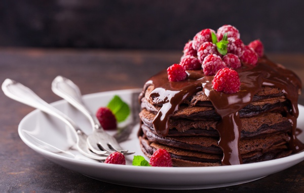 Шоколадные оладьи на тарелке с шоколадом и ягодами малины 