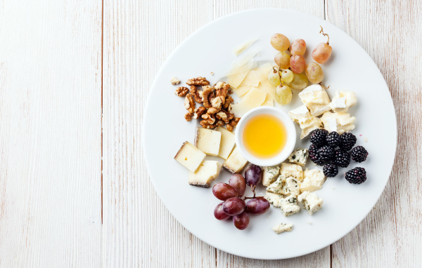 Куски сыра на тарелке с орехами, виноградом, медом и ягодами ежевики