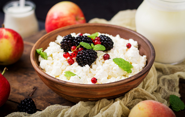 Творог с ягодами в деревянной миске на столе с яблоками