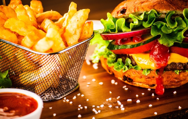 Аппетитный сочный гамбургер на доске с картошкой фри и соусом