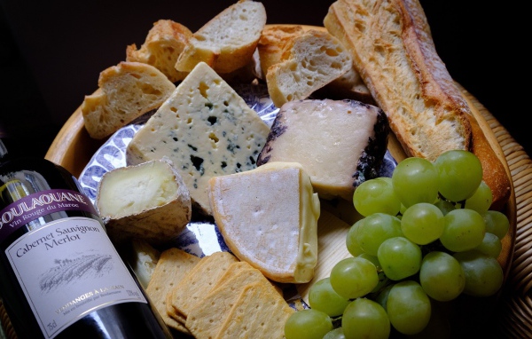 Разные виды твердого сыра на тарелке с белыми виноградом и вином