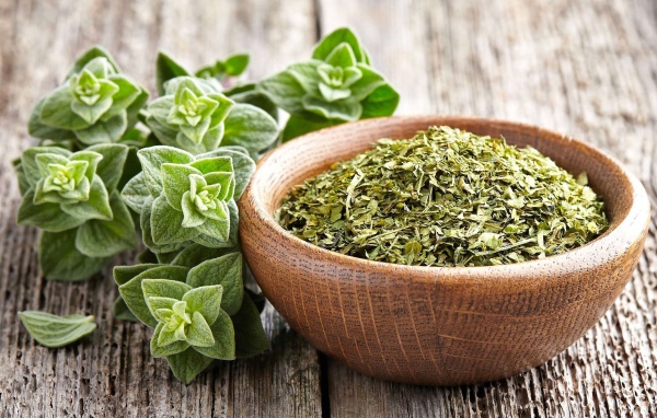 Сухая трава орегано в деревянной миске на столе 