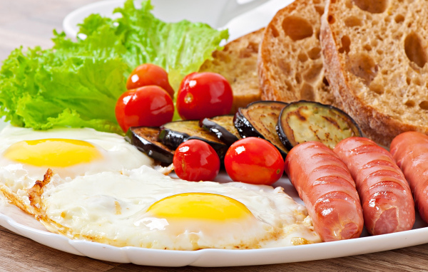 Яичница на тарелке с сосисками, овощами и хлебом
