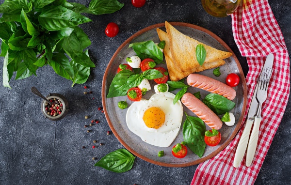 Яичница на тарелке с помидорами, гренками, сыром, сосисками и зеленью базилика