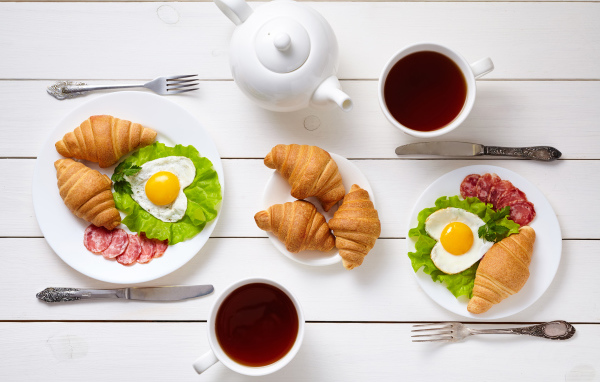 Яичница с колбасой и круассанами на столе чаем 