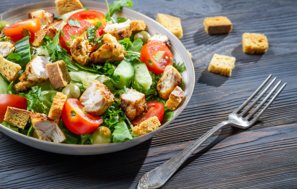 Салат с овощами, сухариками и курицей и на столе с вилкой