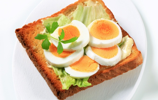 Тост с листом салата и кусочками яйца на белой тарелке 