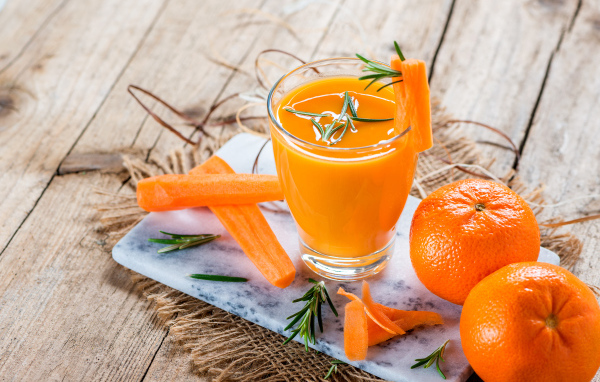 Два апельсина на столе со стаканом морковного сока