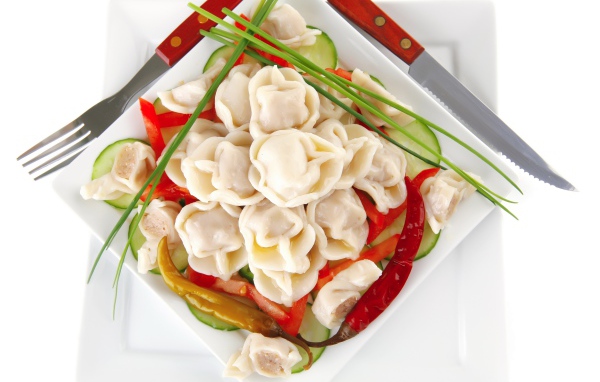 Белая тарелка с пельменями, красным перцем и огурцами