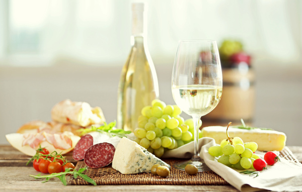 Белое вино на столе с сыром, колбасой и виноградом