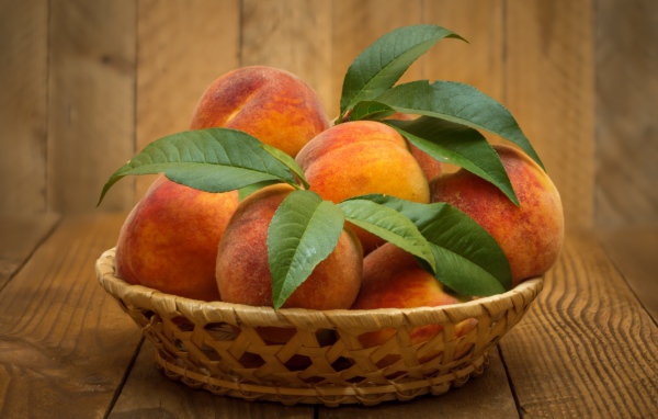 Корзинка персиков с зелеными листьями на столе